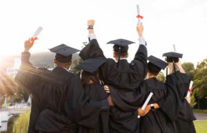 A group of university students in cap and gown raising their diplomas upon graduating.